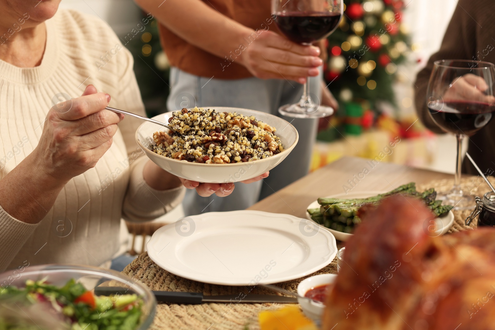 Photo of Woman with bowl of traditional Christmas kutia and her family at festive dinner, closeup. Slavic dish