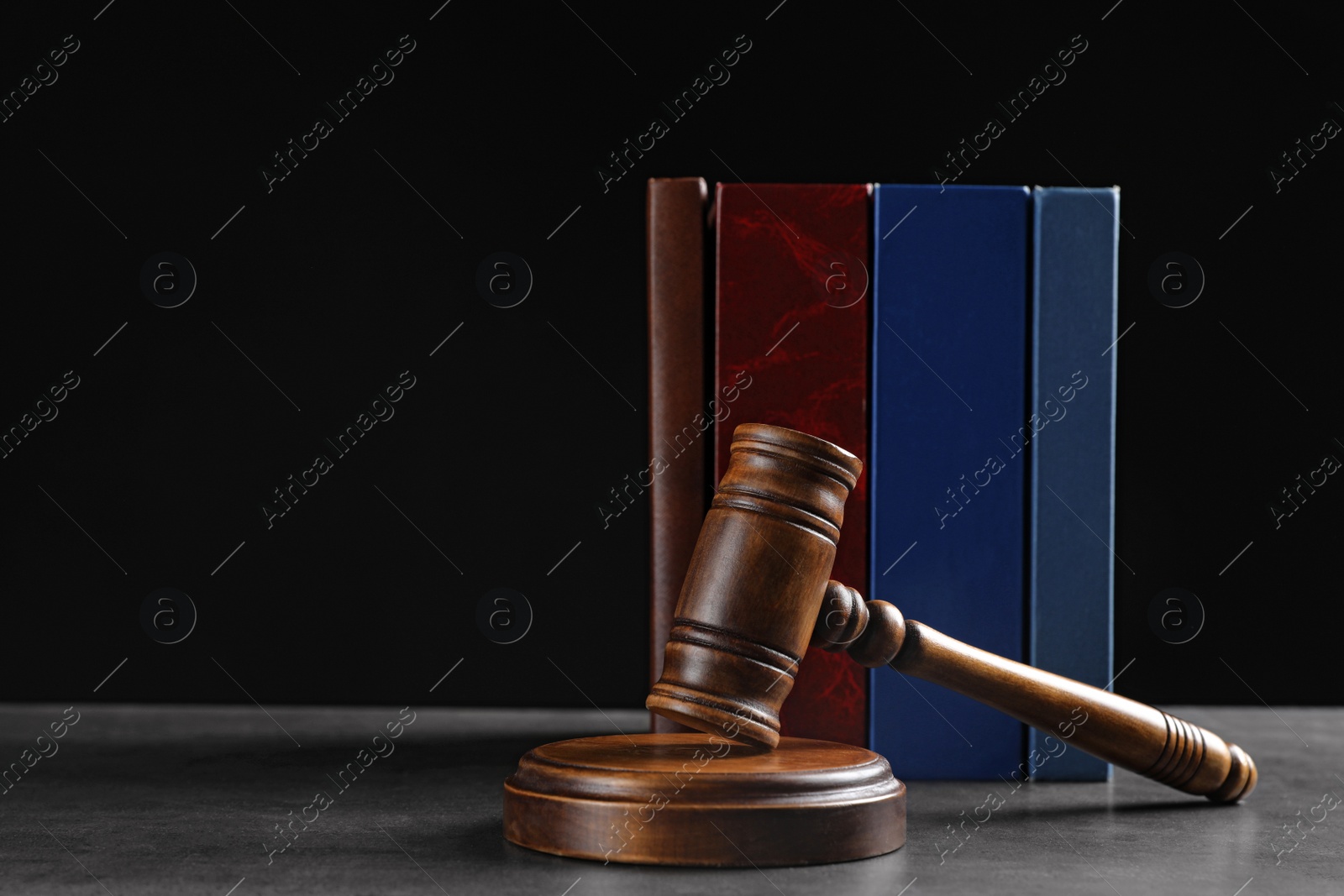 Photo of Judge's gavel and books on grey table against black background, space for text. Criminal law concept