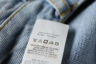 Photo of Clothing label with care symbols and material content on blue jeans, closeup view