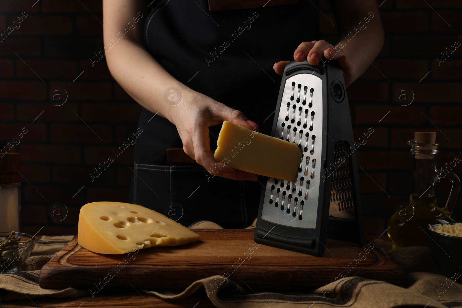 Photo of Woman grating cheese at wooden table, closeup