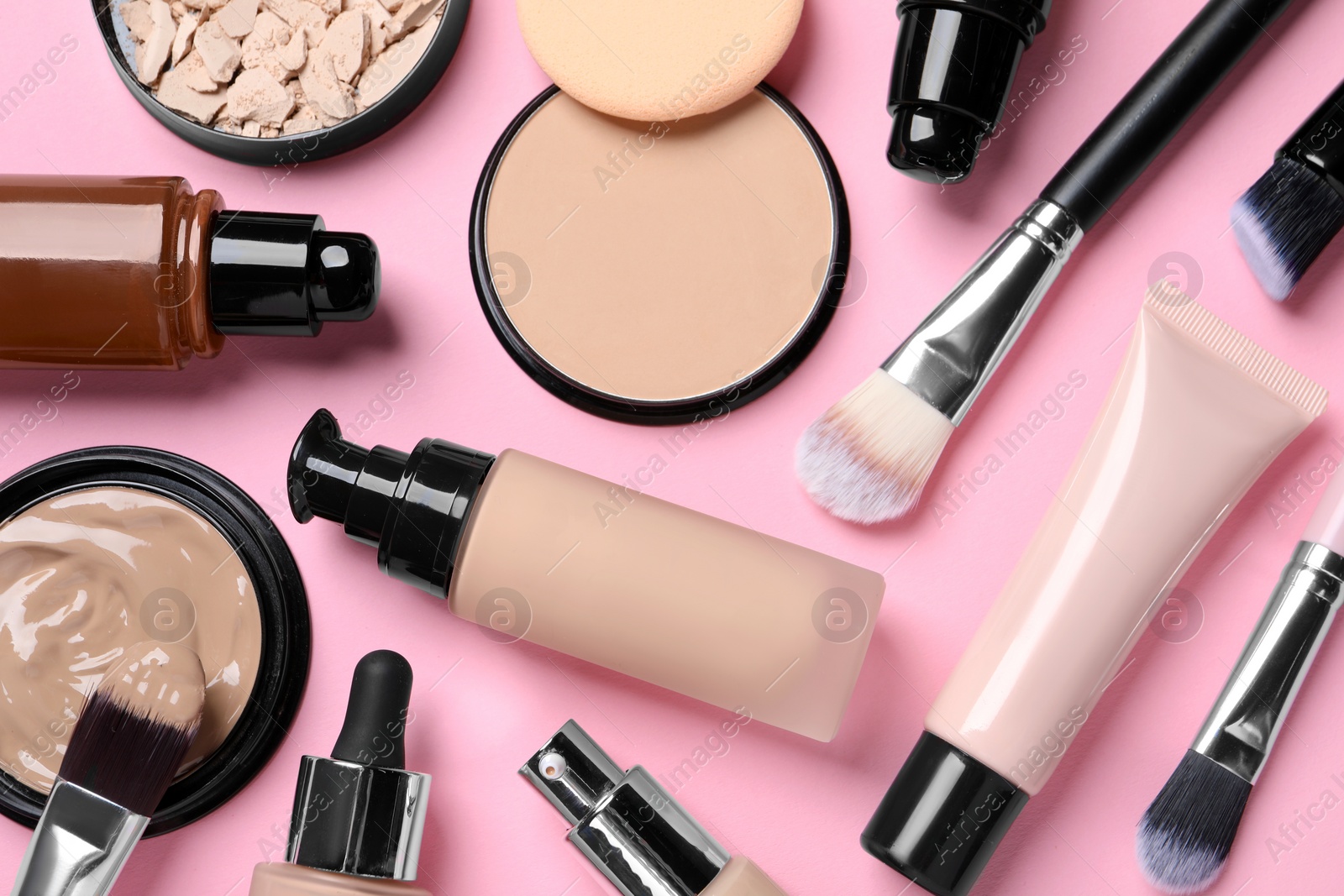 Photo of Different liquid foundations, beauty accessories and face powders on pink background, flat lay