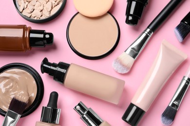 Different liquid foundations, beauty accessories and face powders on pink background, flat lay