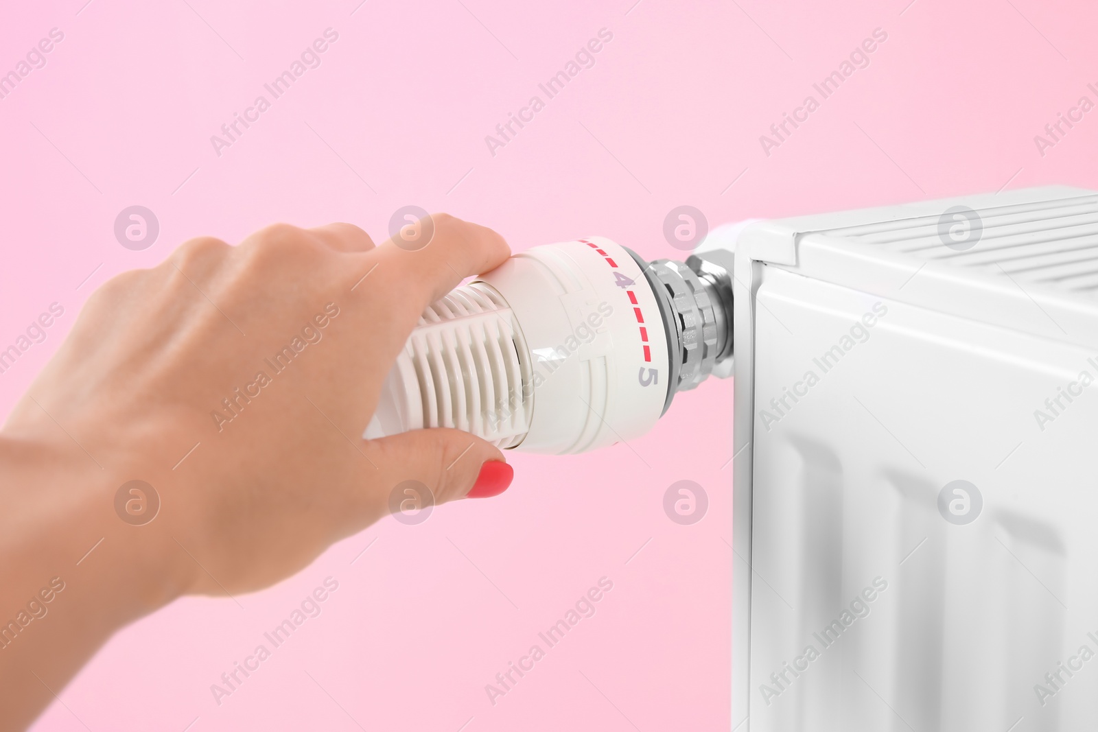 Photo of Woman adjusting heating radiator thermostat near color wall