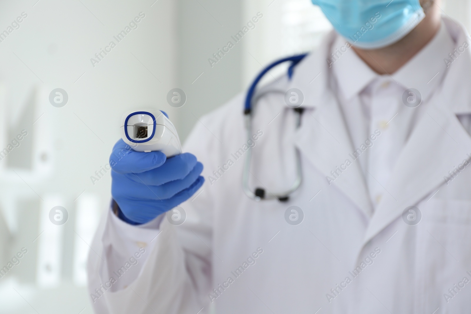 Photo of Doctor holding non contact infrared thermometer indoors, focus on hand. Measuring temperature