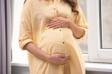 Beautiful pregnant woman near window at home