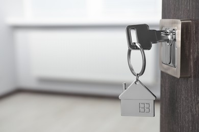 Photo of Mortgage and real estate. Open door with key and house shaped keychain against blurred background, space for text