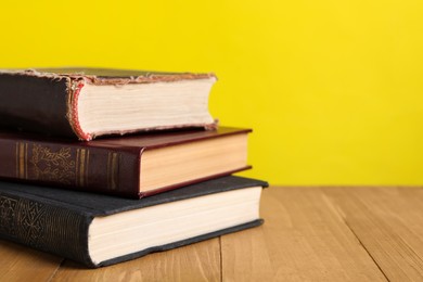 Stack of old hardcover books on wooden table against yellow background, closeup. Space for text