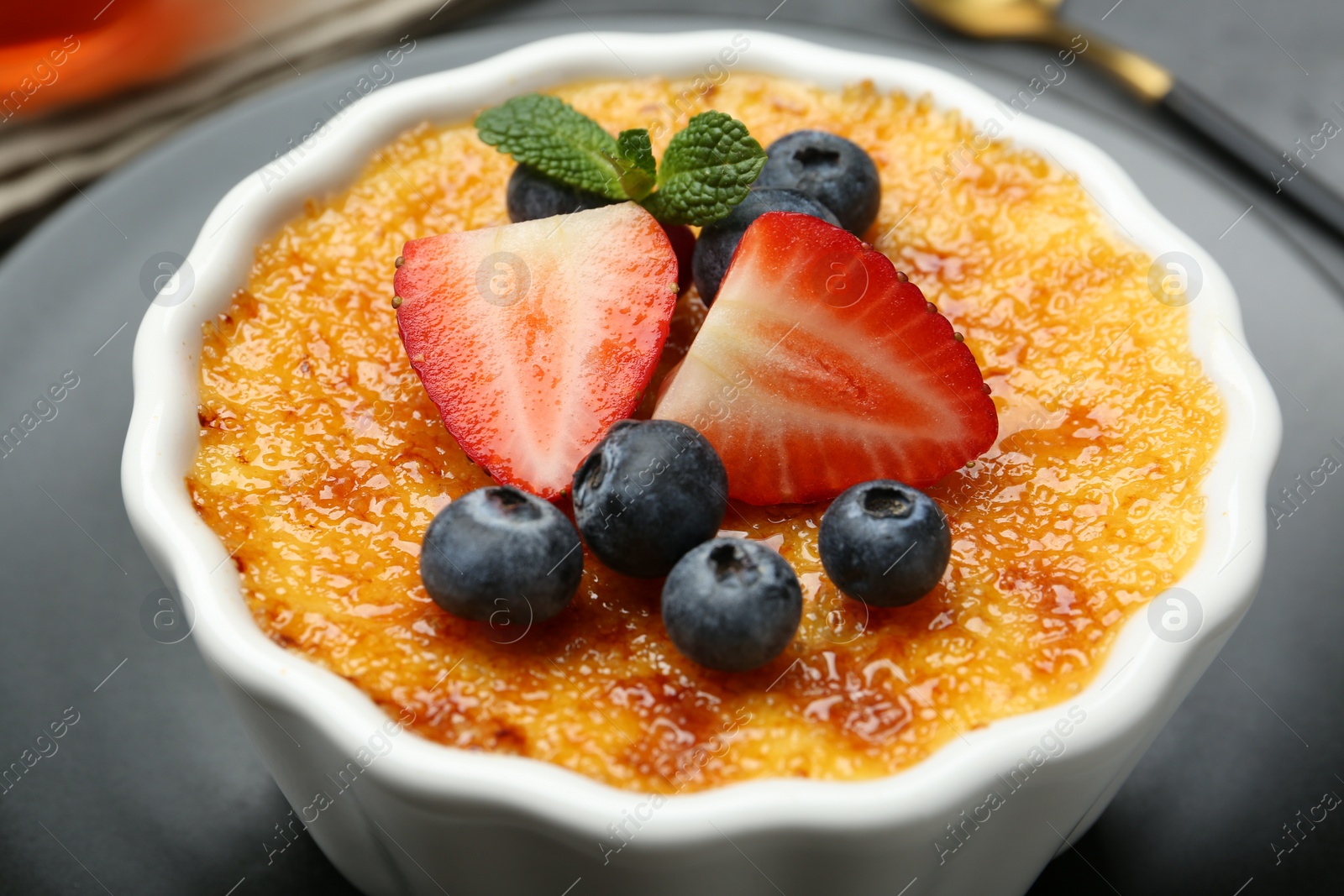 Photo of Delicious creme brulee with berries and mint in bowl on plate, closeup