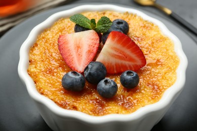 Delicious creme brulee with berries and mint in bowl on plate, closeup