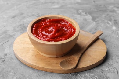 Photo of Organic ketchup in wooden bowl and spoon on grey textured table. Tomato sauce