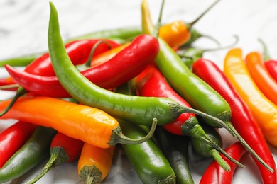 Photo of Different ripe chili peppers on marble table, closeup