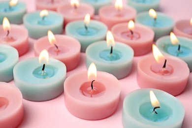 Burning colorful decorative candles on pink background, space for text