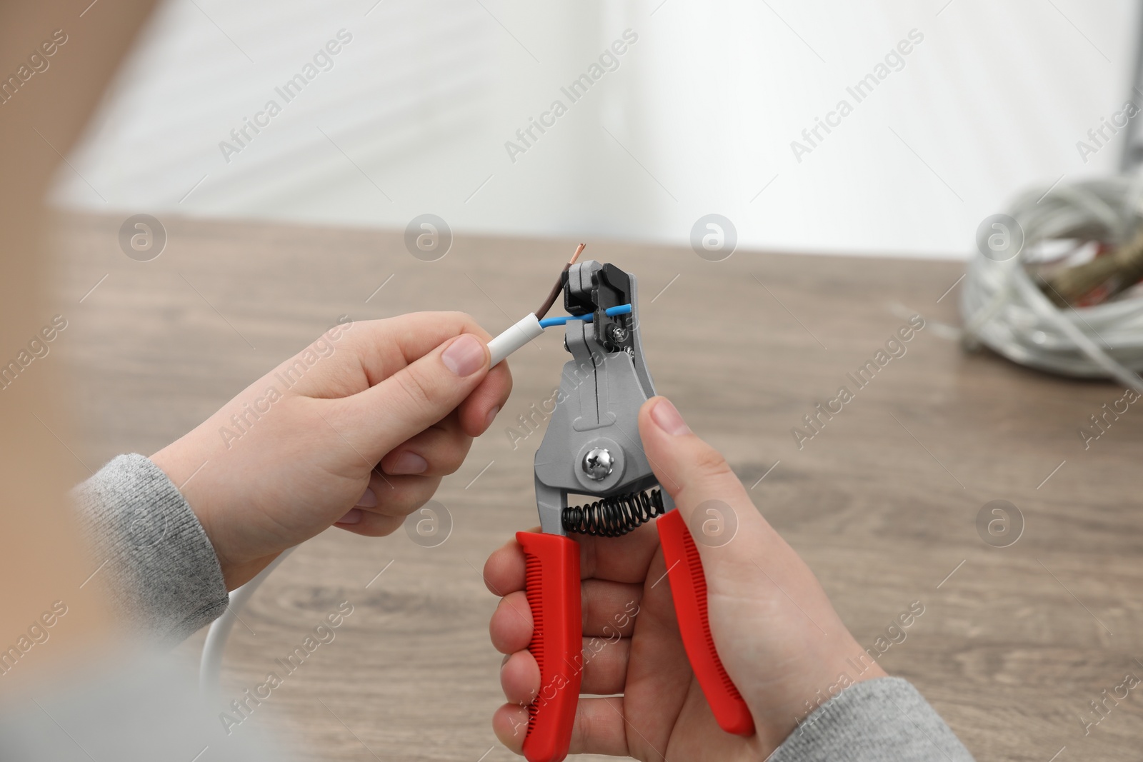 Photo of Professional electrician stripping wiring at wooden table, closeup view