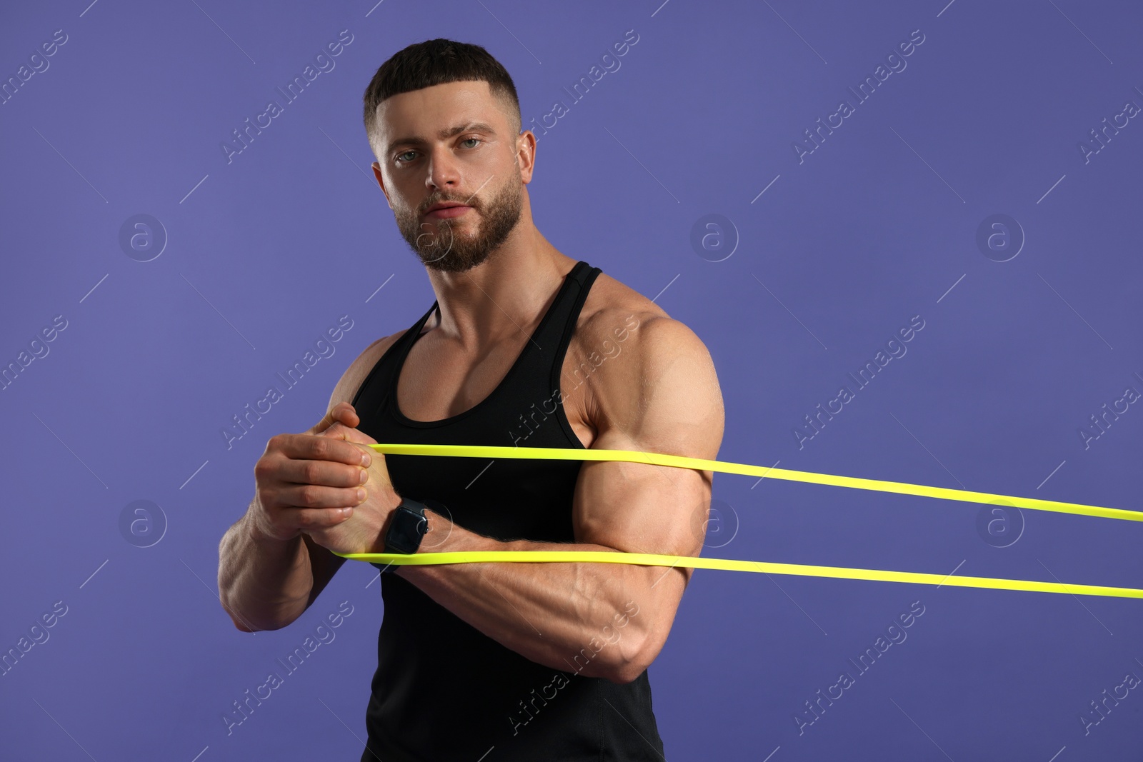 Photo of Muscular man exercising with elastic resistance band on purple background