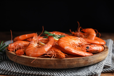 Delicious cooked shrimps on wooden plate against black background