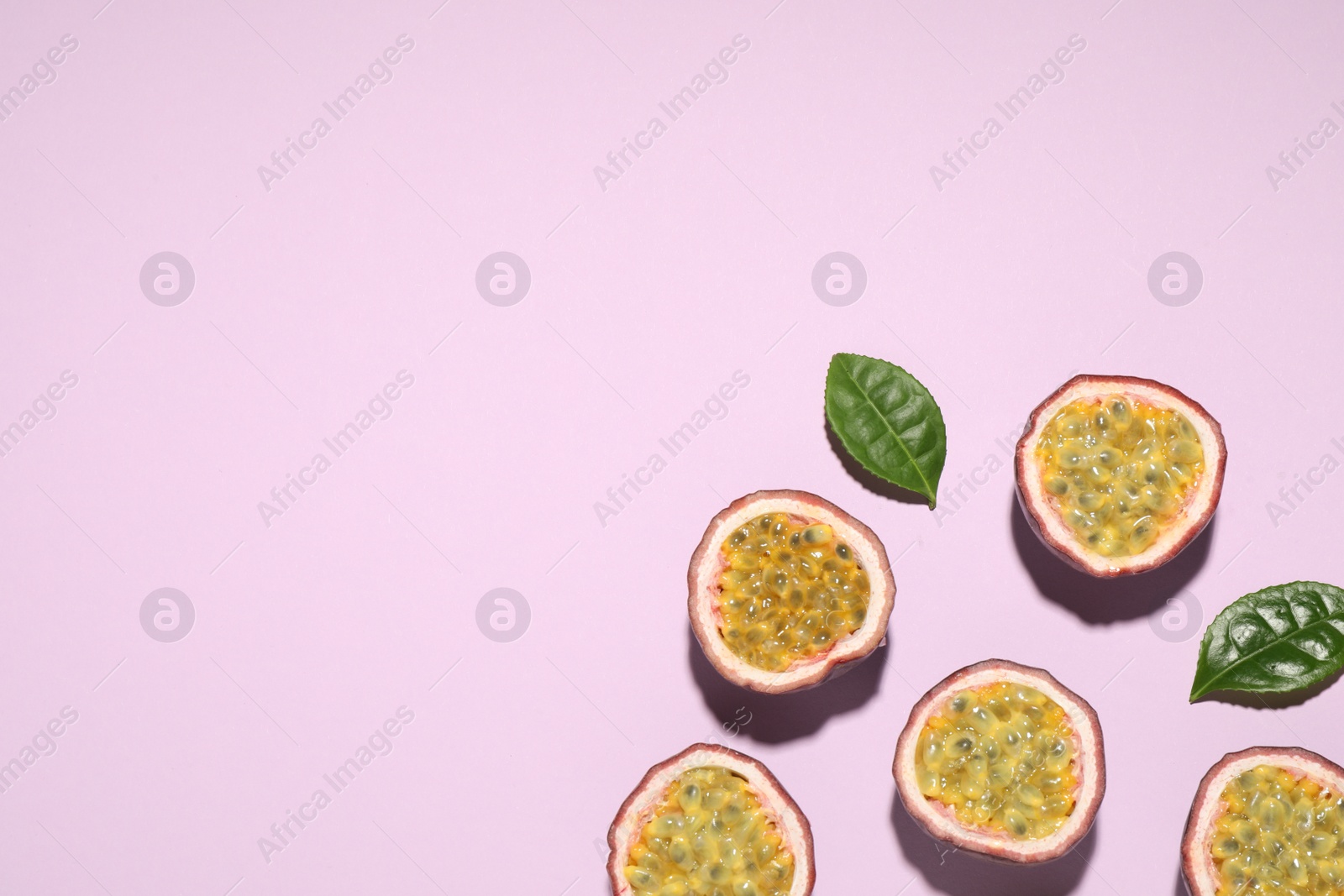 Photo of Halves of passion fruits (maracuyas) and green leaves on pink background, flat lay. Space for text