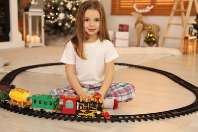 Little girl playing with colorful train toy in room decorated for Christmas