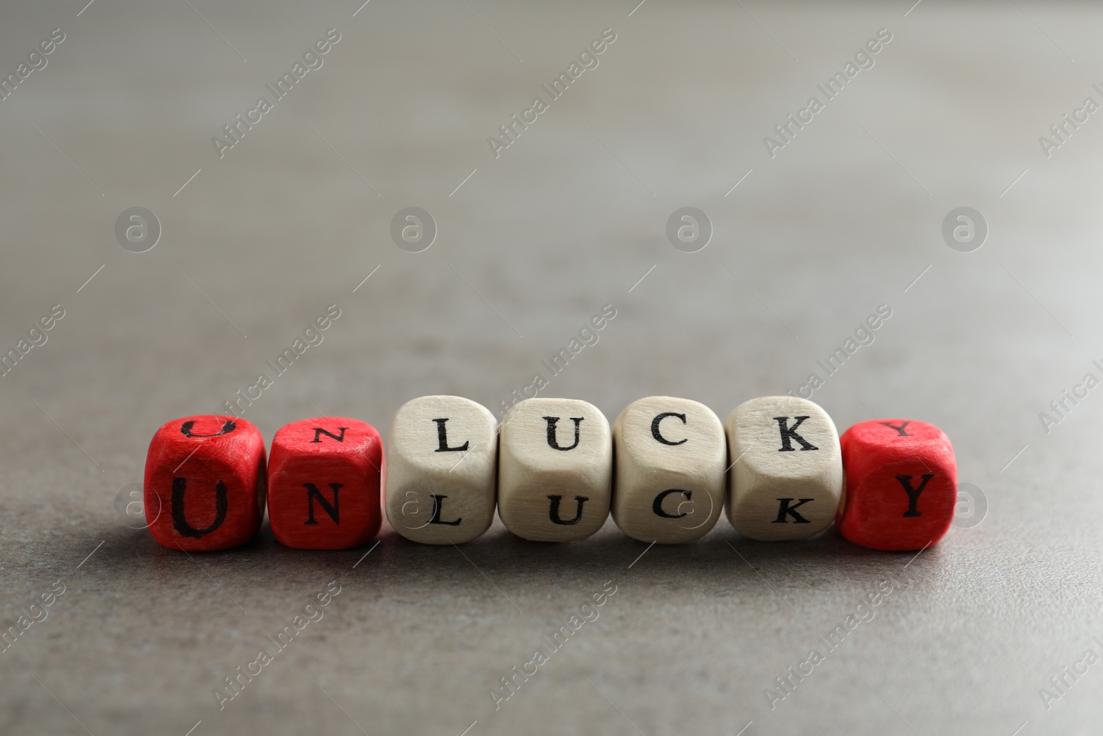 Photo of Red and white cubes with word UNLUCKY on light grey stone table, closeup