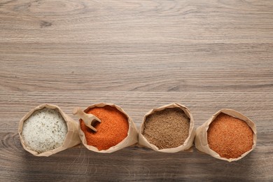 Photo of Different kinds of salt in paper bags on wooden table, flat lay. Space for text