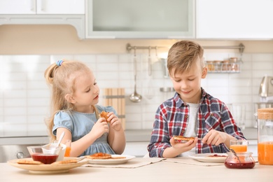 Photo of Cute little children eating tasty toasted bread with jam at table in kitchen