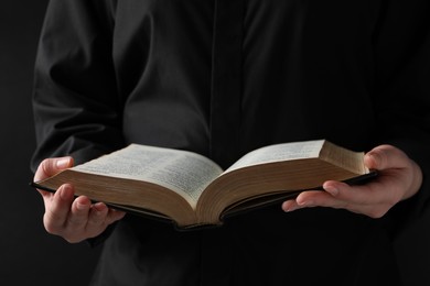 Woman reading holy Bible on black background, closeup
