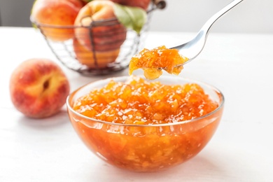 Photo of Bowl and spoon with peach jam on table