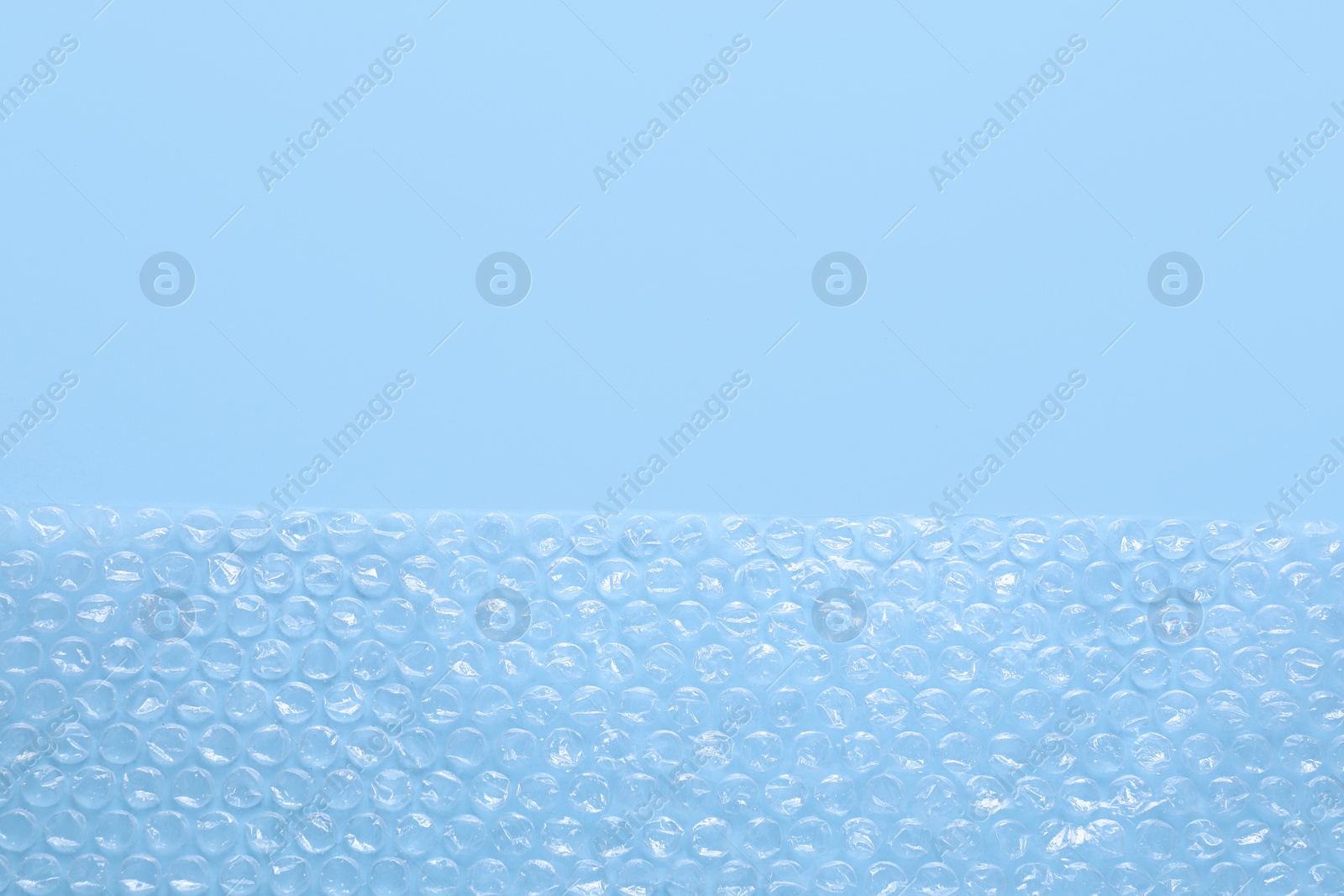 Photo of Transparent bubble wrap on light blue background, top view. Space for text