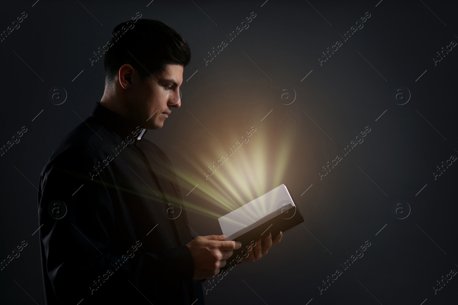 Image of Priest holding Bible with holy light on black background