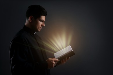 Image of Priest holding Bible with holy light on black background
