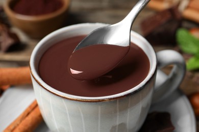 Photo of Spoon with yummy hot chocolate over cup, closeup