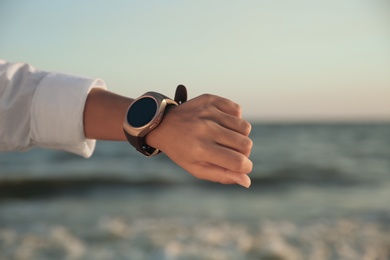 Photo of Young woman checking smart watch on beach at sunset, closeup