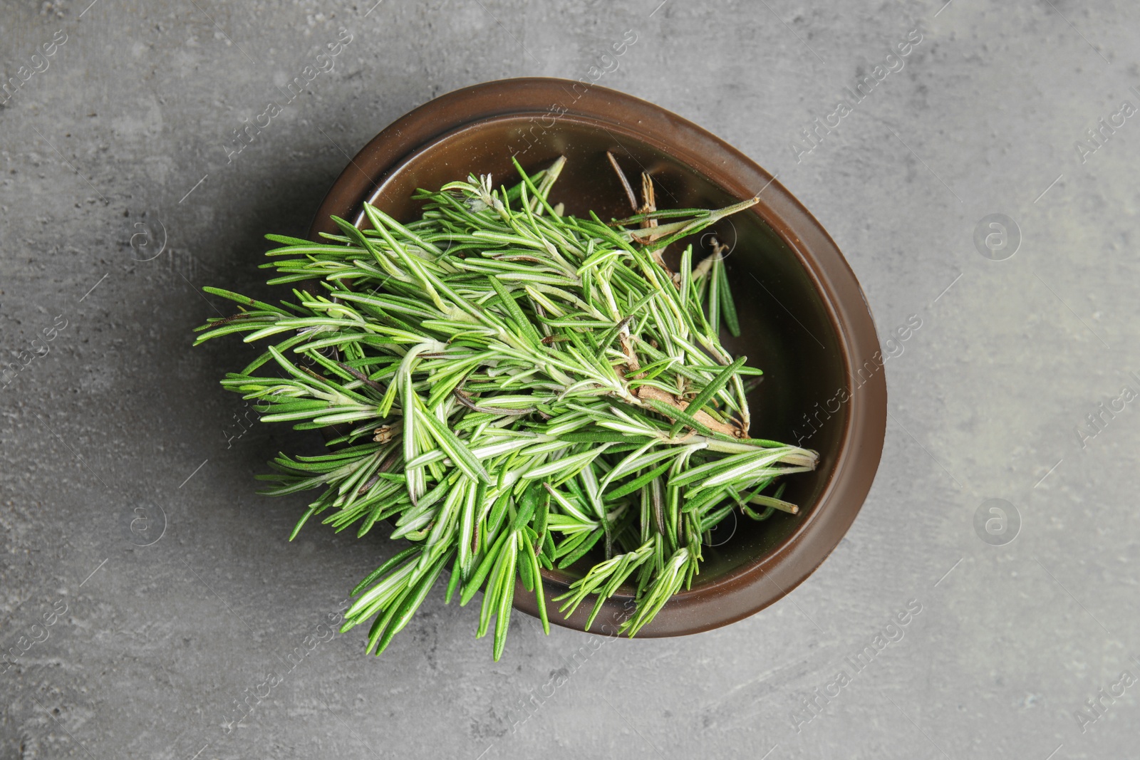 Photo of Bowl of fresh green rosemary on grey table, top view