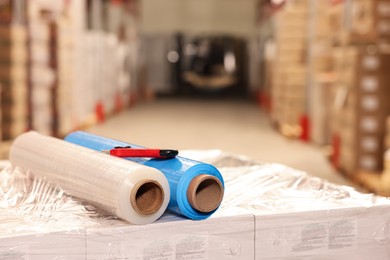 Photo of Rolls of different stretch wraps and utility knife on boxes in warehouse