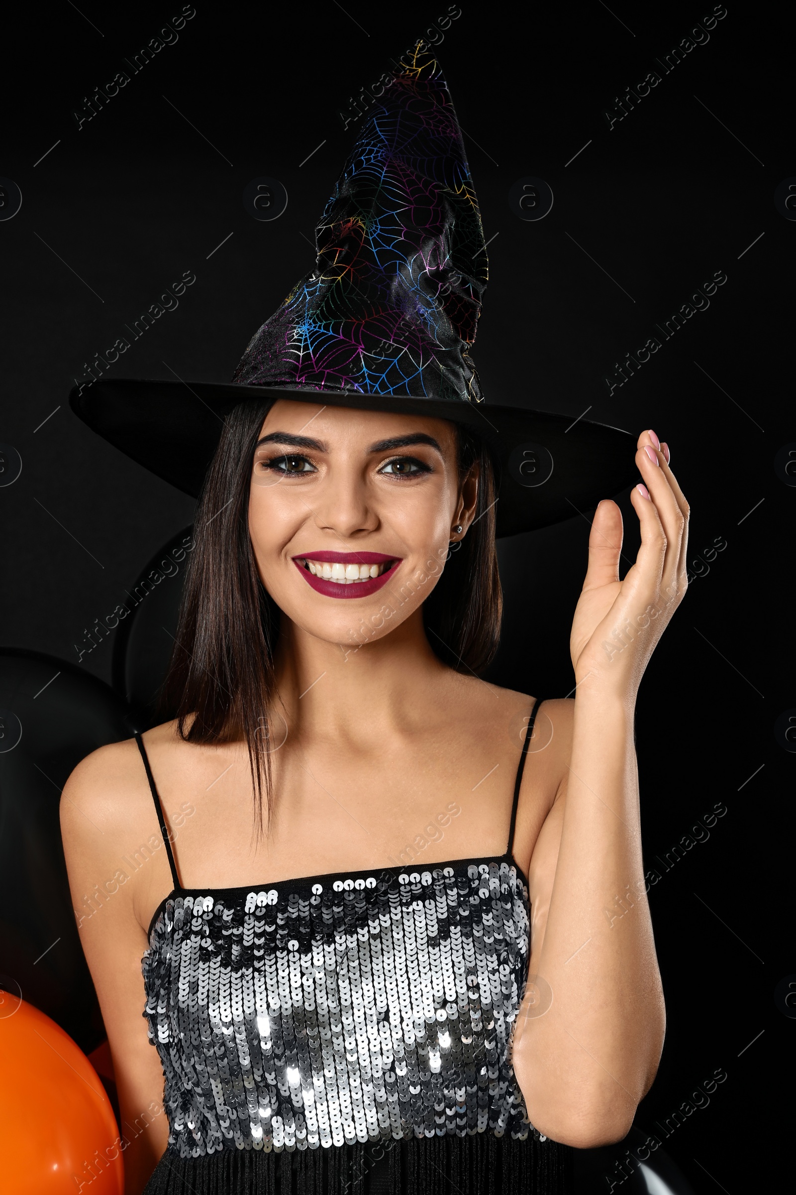 Photo of Beautiful woman wearing witch costume with balloons for Halloween party on black background