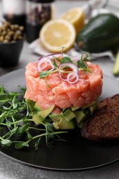 Photo of Tasty salmon tartare with avocado, microgreens and croutons on grey table, closeup