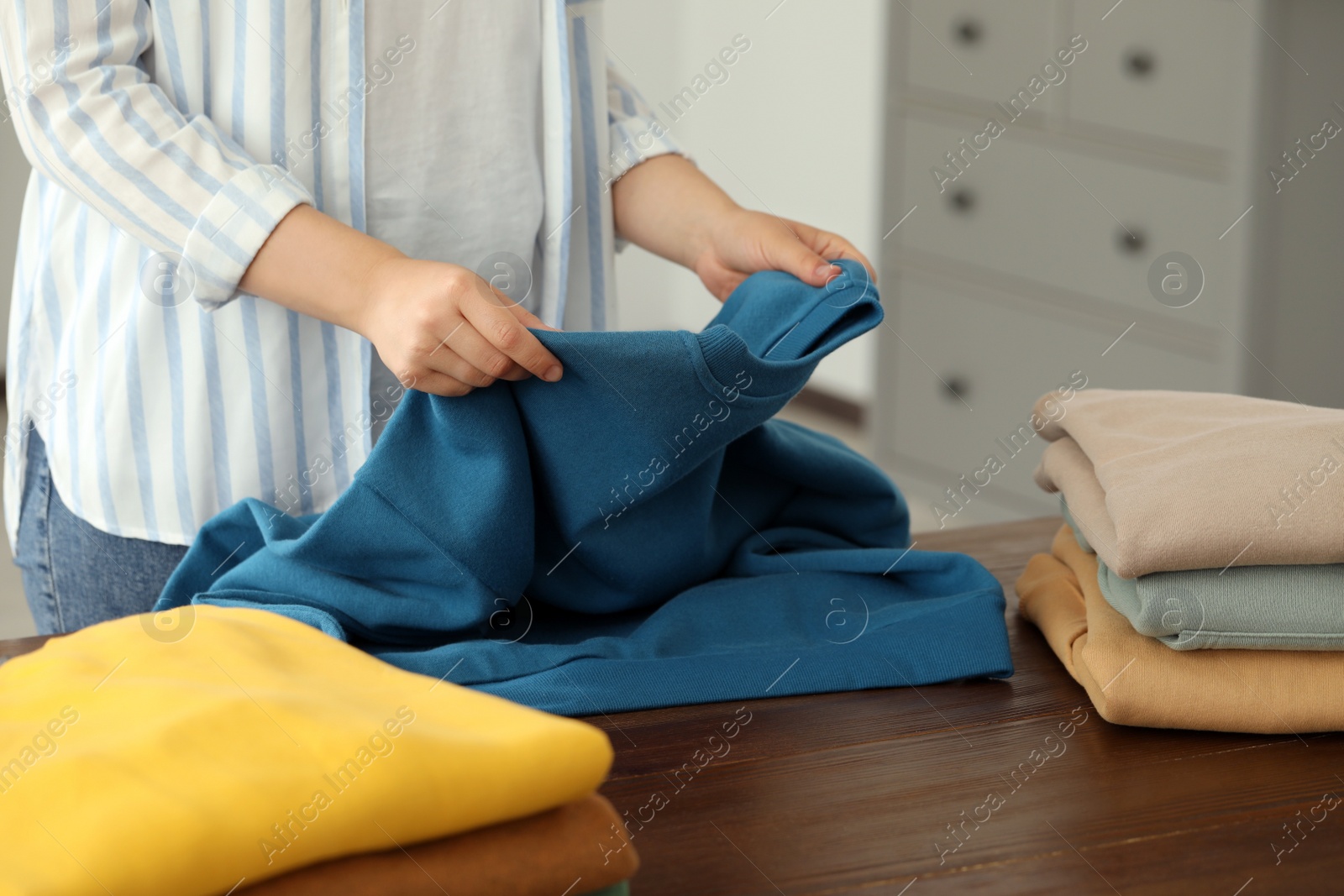 Photo of Woman folding clothes at wooden table indoors, closeup