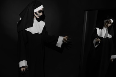 Scary devilish nun near mirror on black background. Halloween party look