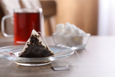 Photo of Glass saucer with used tea bag on wooden table