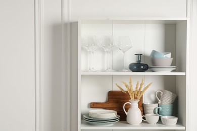 Photo of Different ceramic dishware and glasses on shelves in cabinet indoors. Space for text