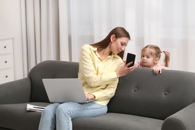 Photo of Mother giving smartphone to her daughter at home. Woman hoping to keep child busy while she will work remotely
