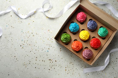 Photo of Box with delicious colorful cupcakes, ribbon and confetti on light grey table, flat lay. Space for text