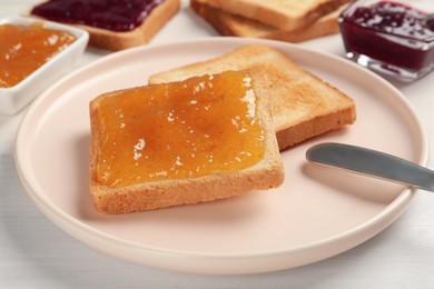 Toast with tasty orange jam, roasted slice of bread and knife on plate, closeup