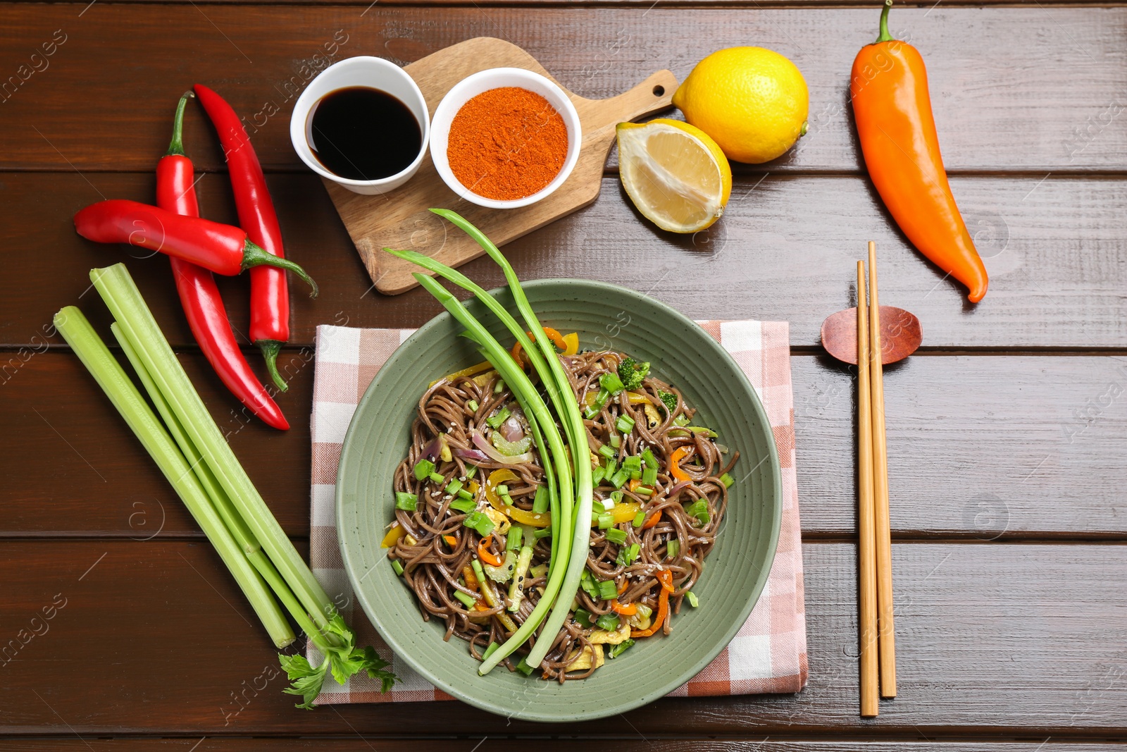 Photo of Stir-fry. Delicious cooked noodles with chicken and vegetables in bowl on wooden table, flat lay