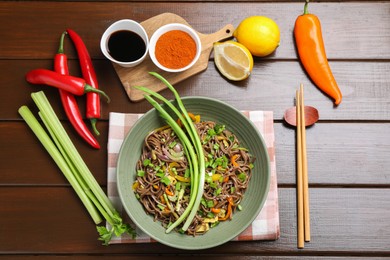 Photo of Stir-fry. Delicious cooked noodles with chicken and vegetables in bowl on wooden table, flat lay