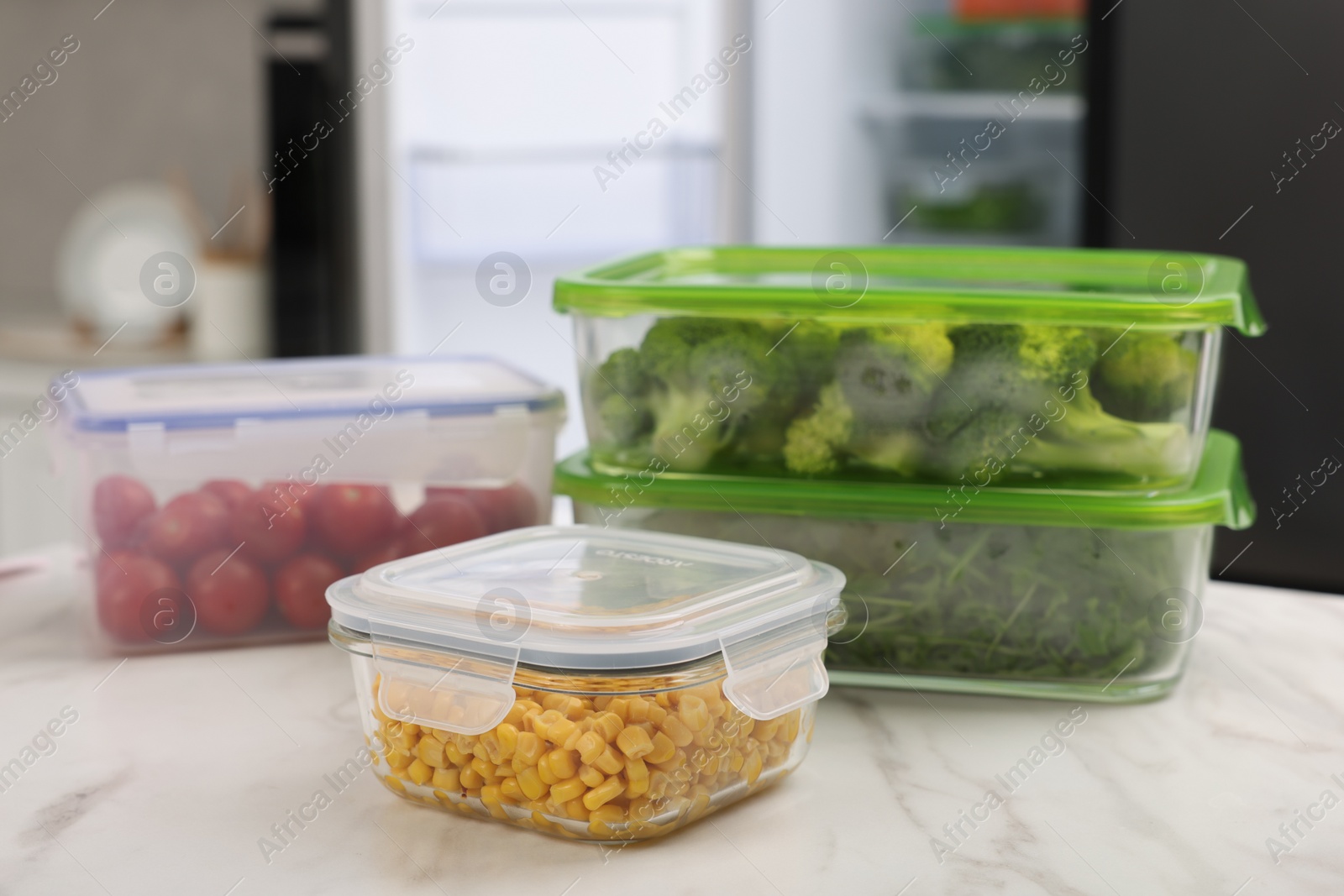 Photo of Glass and plastic containers with different fresh products on white marble table in kitchen. Food storage