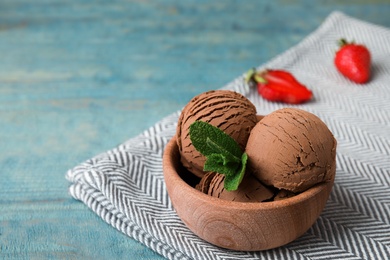 Photo of Wooden bowl of chocolate ice cream, mint and strawberry on table, space for text