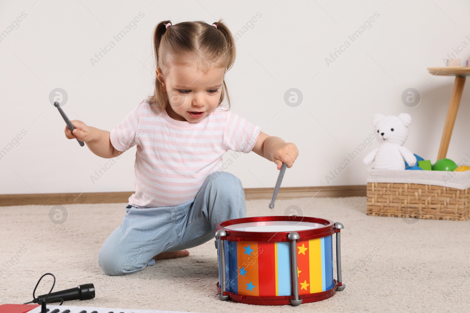 Photo of Cute little girl playing with drum, drumsticks and toy piano at home