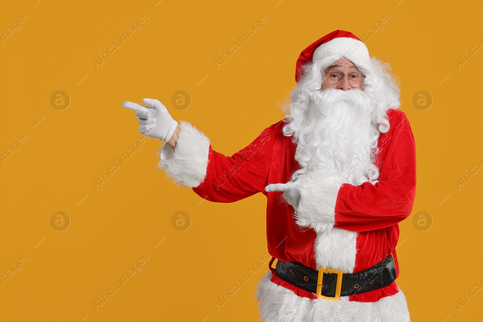 Photo of Merry Christmas. Santa Claus pointing at something on orange background, space for text