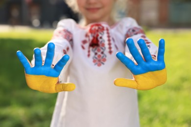 Photo of Little girl with hands painted in Ukrainian flag colors outdoors, closeup. Love Ukraine concept