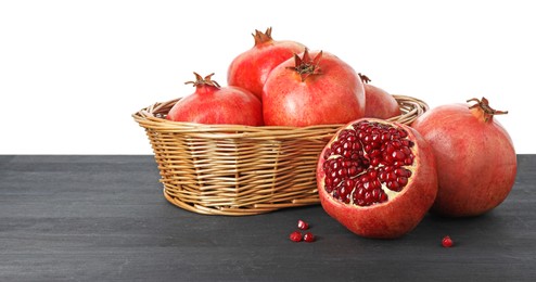 Fresh pomegranates in wicker basket on black wooden table against white background, space for text